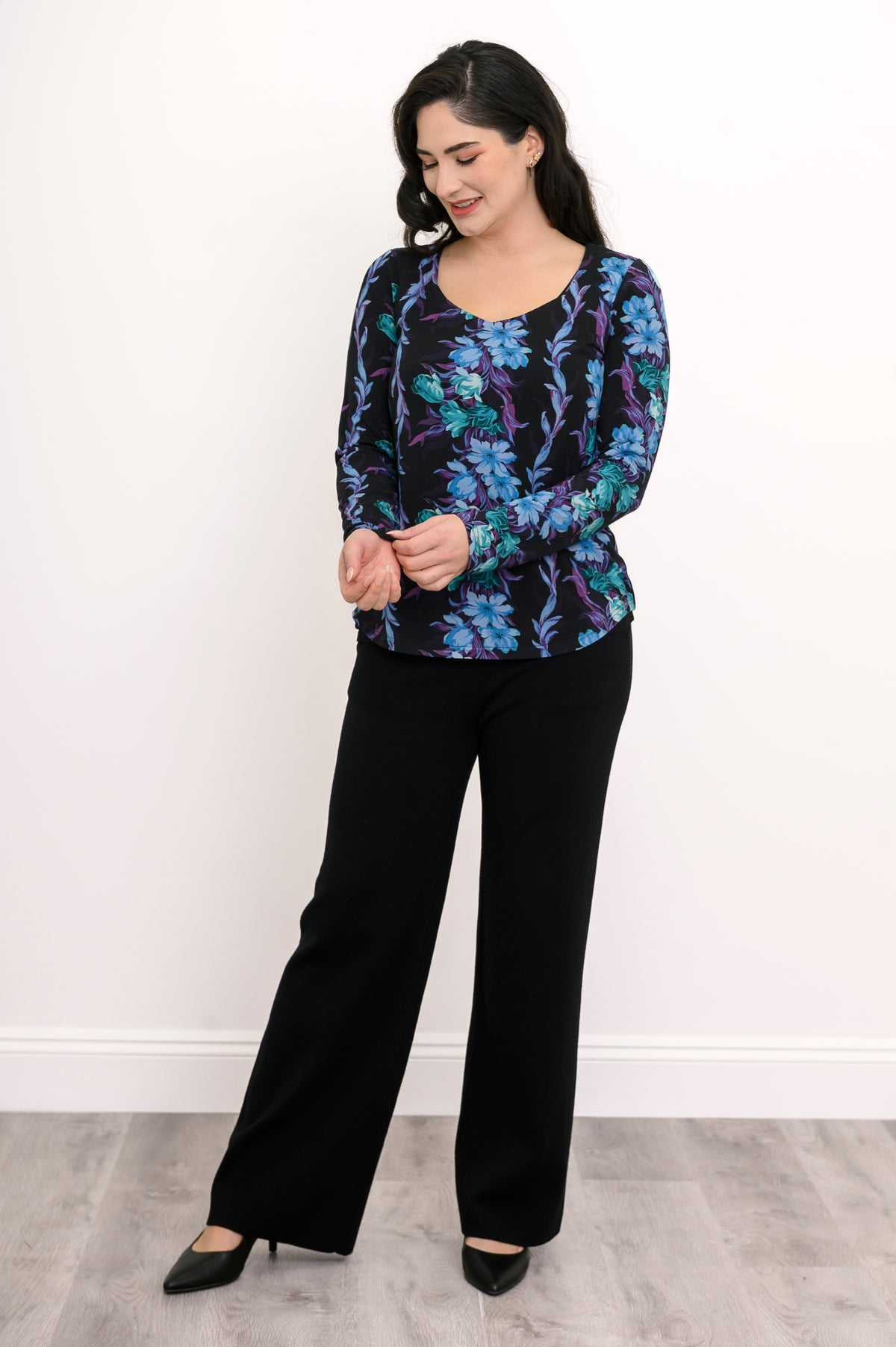 Smiling woman posing in a teal and black floral patterned bamboo-blend top with long sleeves, front view.