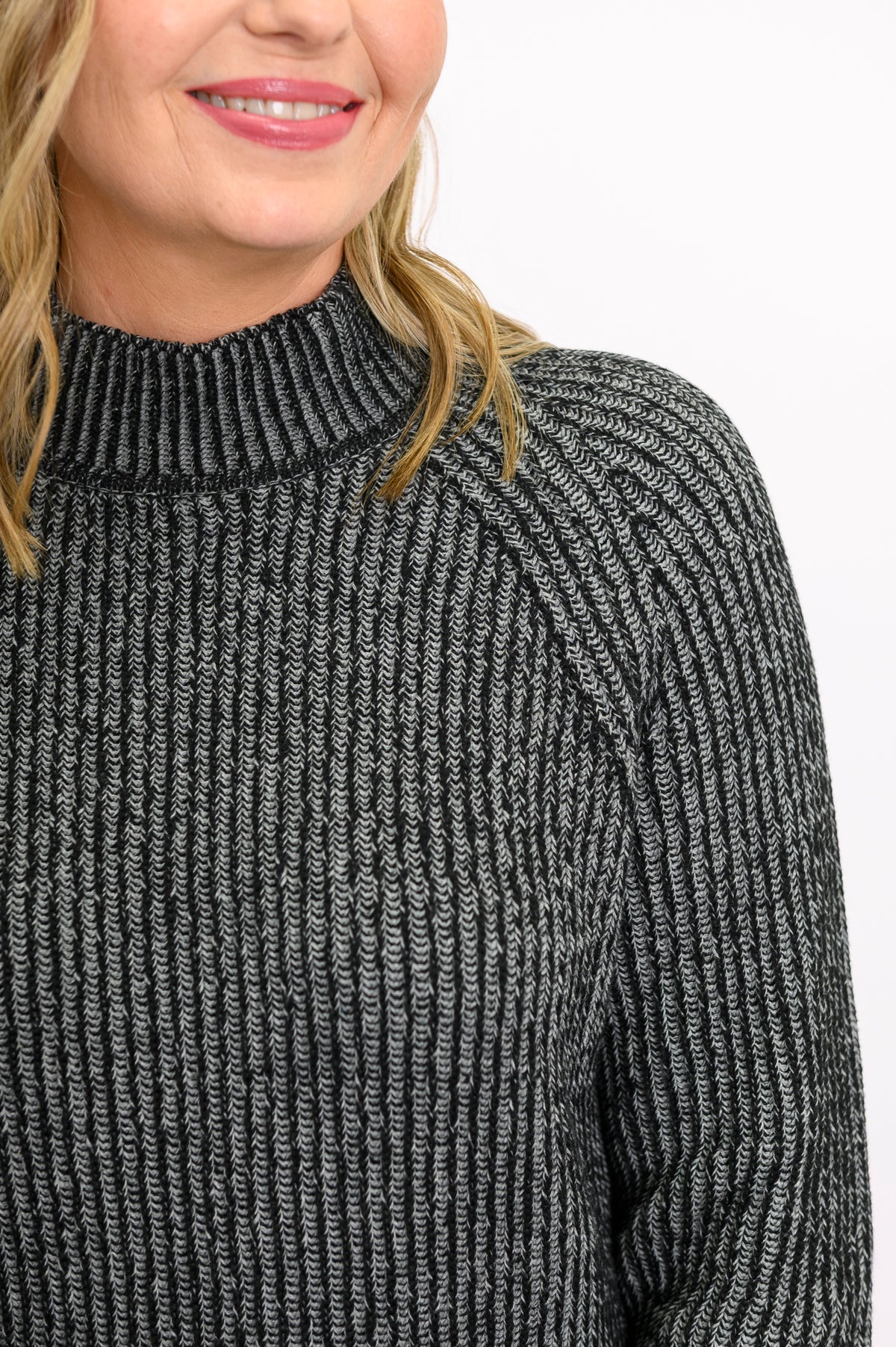 Close-up of a charcoal gray cotton sweater, highlighting the textured two-tone stitch and low mock neck collar.