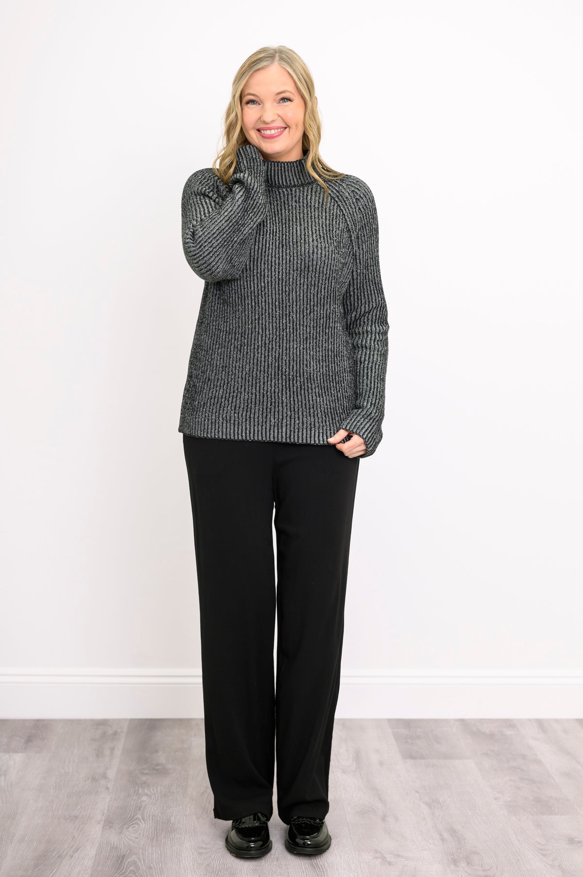 Smiling woman posing in a dark gray mock neck sweater with long sleeves, showing a casual front-facing look.