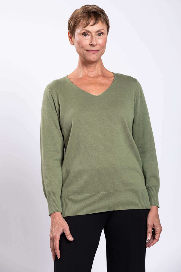 Woman wearing a sage green V-neck cotton sweater with ribbed cuffs and black pants