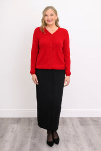Full length view of a woman wearing a red v-neck wool cashmere cardigan paired with a midi black skirt.