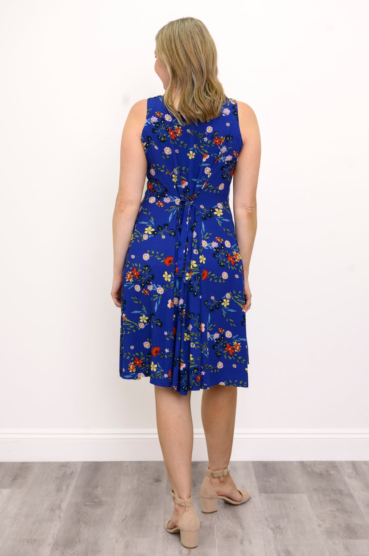 Back view of woman wearing a blue floral dress and sandals against a white wall 