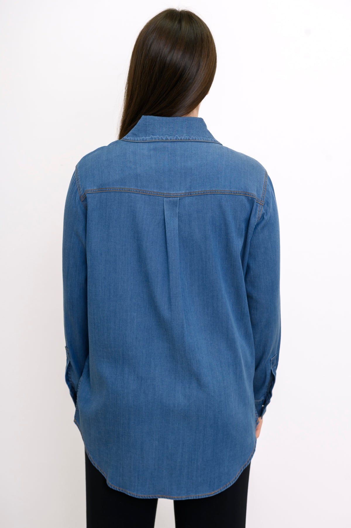 Back close-up view of woman wearing denim shirt with back pleat, collar, and rounded hem