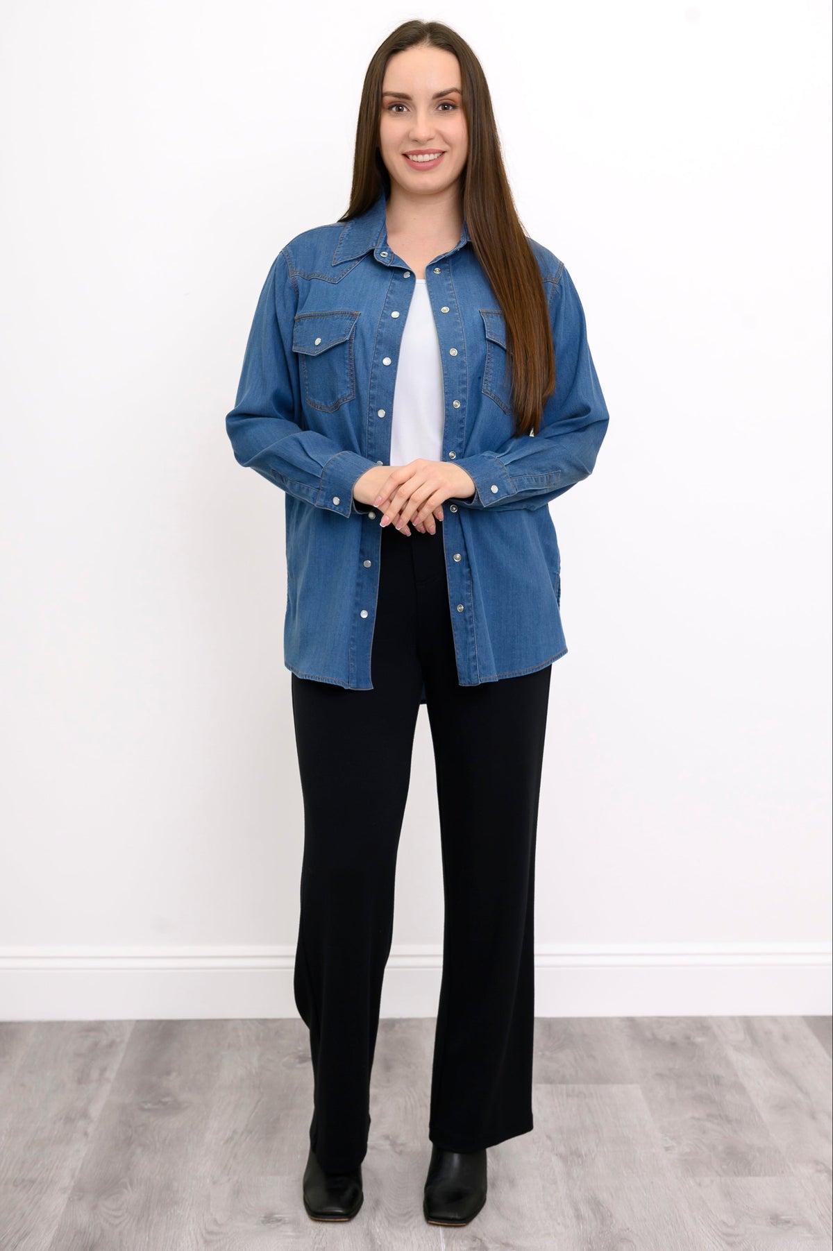 Woman wearing a blue denim shirt over a white top and black pants on a white background, front view