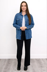 Woman wearing a blue denim shirt over a white top and black pants on a white background, front view