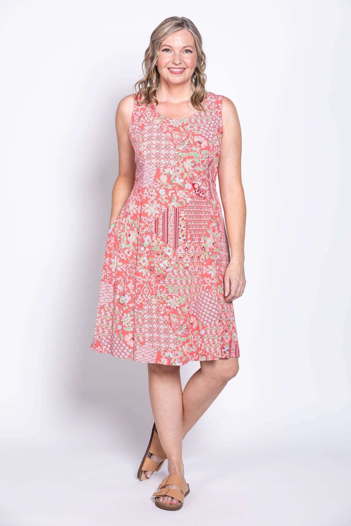 Woman smiling in sleeveless pink patchwork dress with hands in pockets