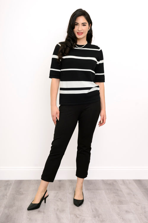 Woman wearing a black and white striped sweater and black pants against a white background, front view