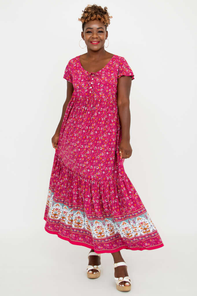Woman in a bright pink flutter sleeve maxi dress with floral border and white sandals