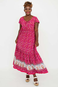 Woman in a bright pink flutter sleeve maxi dress with floral border and white sandals
