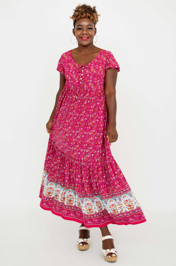 Woman in a bright pink flutter sleeve maxi dress with floral border and white sandals