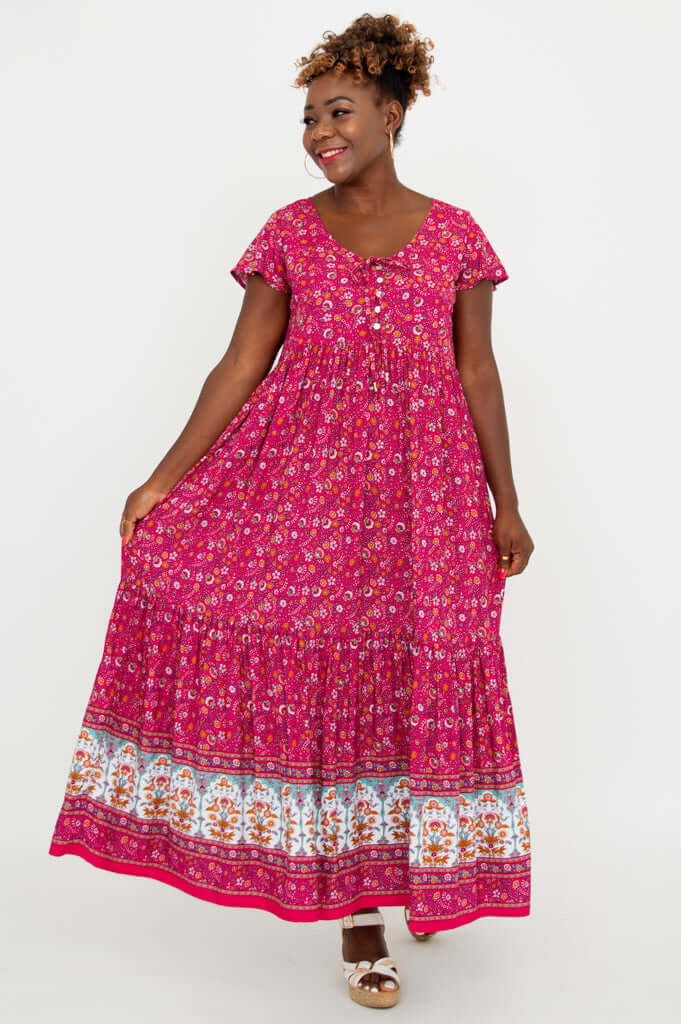 Woman displaying the flow of a pink floral tiered maxi dress with border print and flutter sleeves