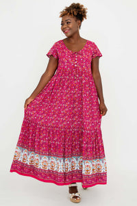 Woman displaying the flow of a pink floral tiered maxi dress with border print and flutter sleeves