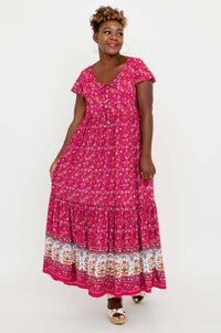 Smiling woman wearing a flutter sleeve maxi dress in pink with floral details and tiered skirt