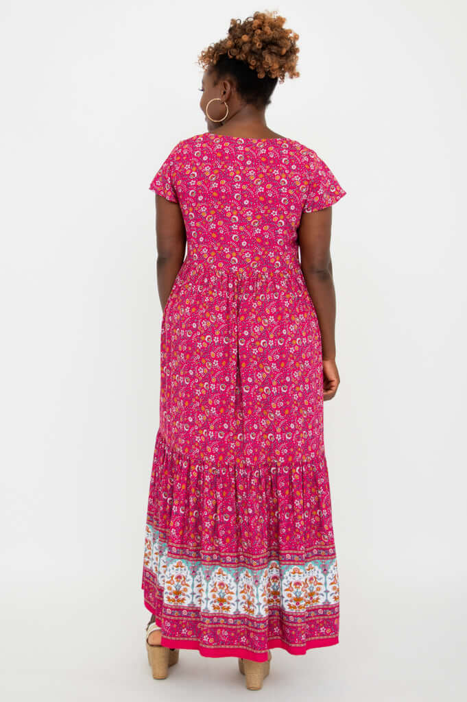 Back view of a woman wearing a pink maxi dress with flutter sleeves and floral border design