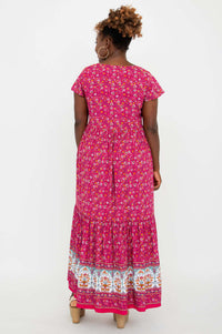 Back view of a woman wearing a pink maxi dress with flutter sleeves and floral border design