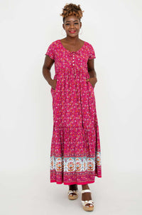 Woman showing pockets in a pink floral maxi dress with a tiered skirt and white sandals