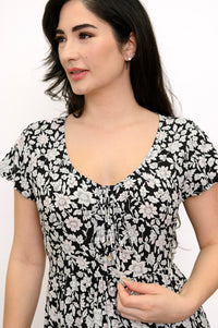 Close-up view of woman wearing black and white floral dress with buttons and tie neckline