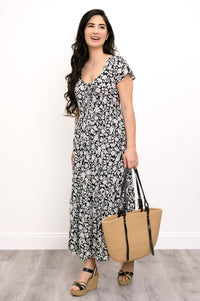 Woman wearing a black and white floral maxi dress, straw bag, and sandals on a white background, front view