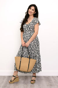 Woman wearing a black and white floral maxi dress, straw bag, and sandals on a white background, front view