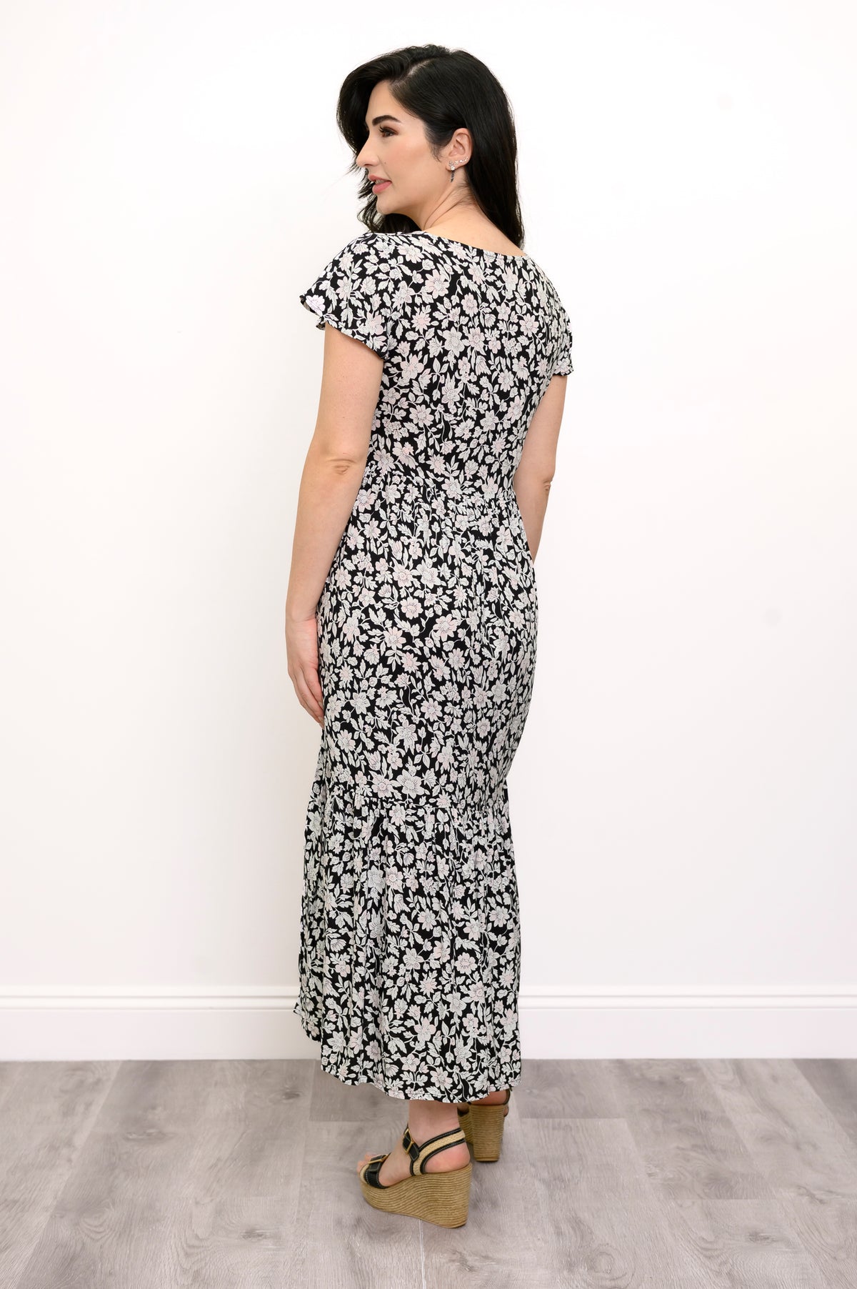 Woman wearing a black and white floral maxi dress and sandals on a white background, back view