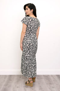 Woman wearing a black and white floral maxi dress and sandals on a white background, back view