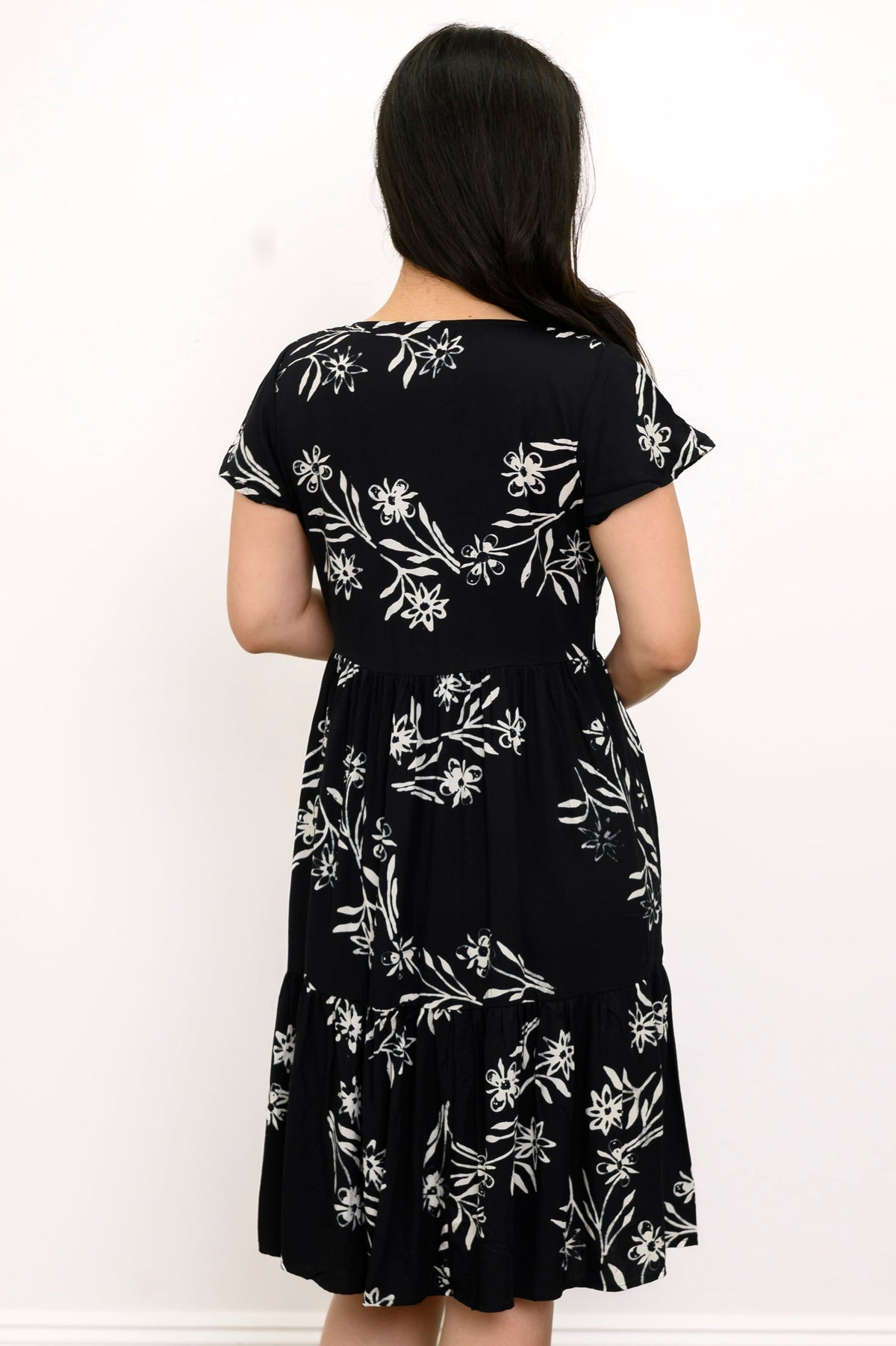 Back view of woman with her hair pushed to the side and wearing a short-sleeve black dress with white flowers on it