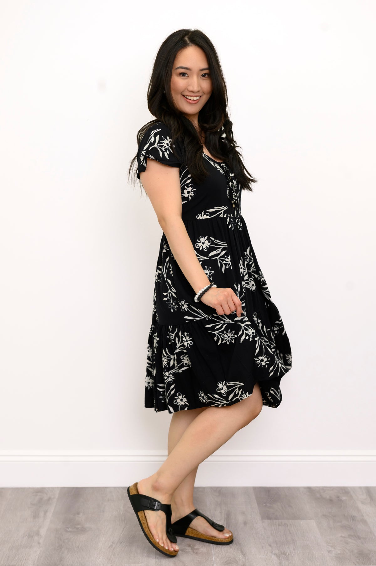 Woman angled slightly to the side and modeling a black short-sleeve floral dress