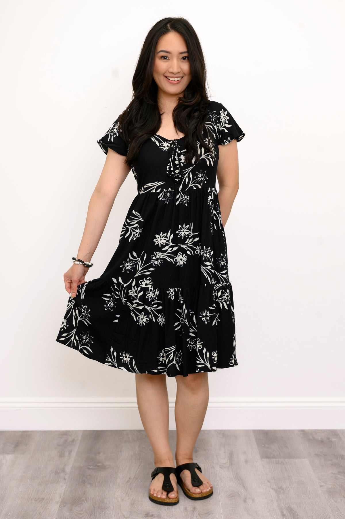 Woman playing with the hem of her flowy black floral dress and looking at the camera