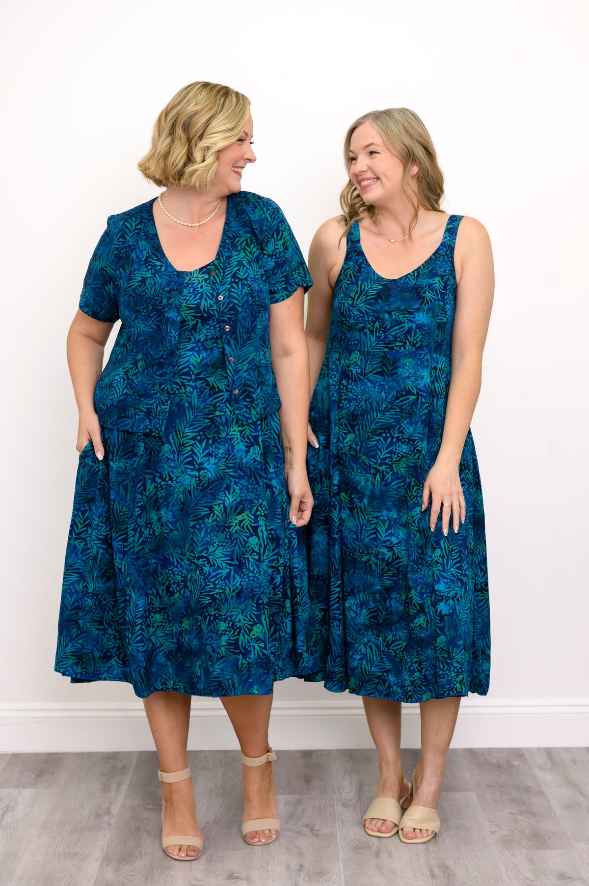 Two women wearing blue patterned dresses standing side by side against a white wall, front view