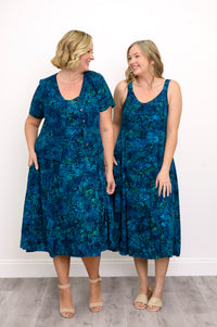 Two women wearing blue patterned dresses standing side by side against a white wall, front view