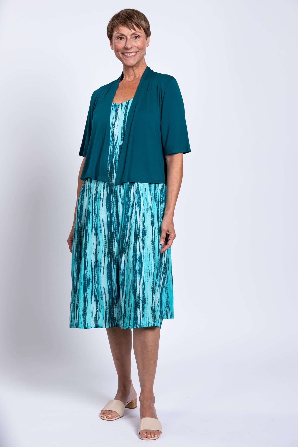 Woman wearing teal streak dress with teal shrug, smiling at camera