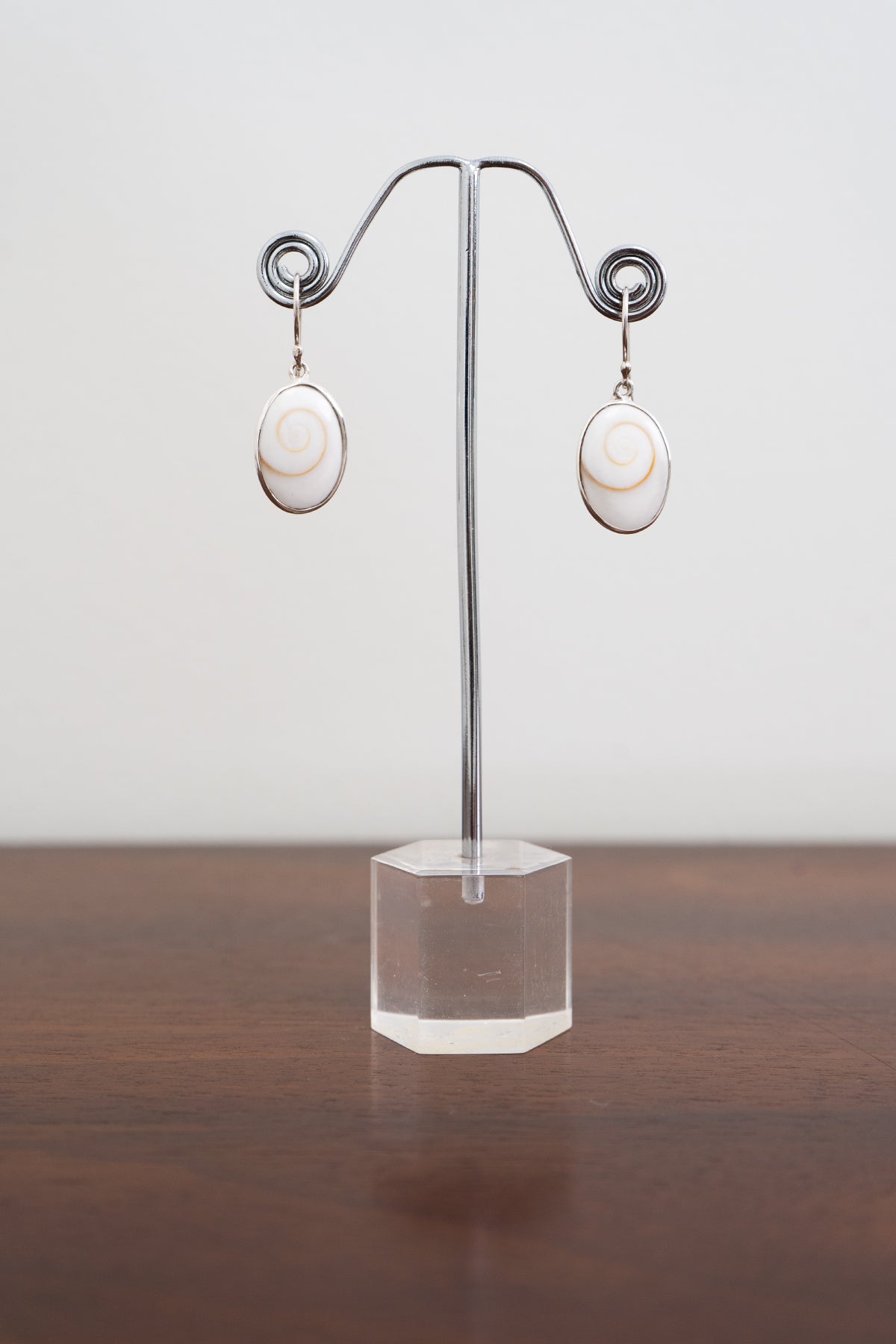 Pair of sterling silver shell earrings on a clear stand against a white background, front view