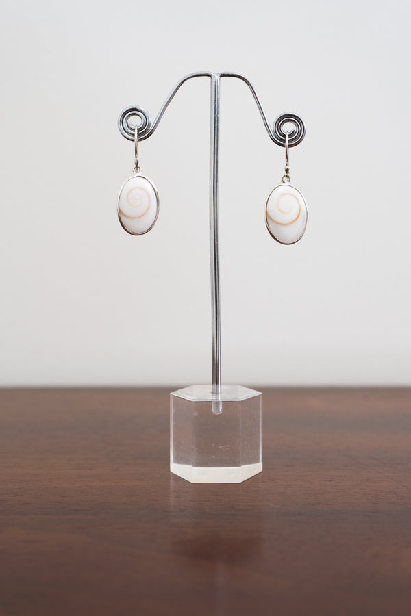 Pair of sterling silver shell earrings on a clear stand against a white background, front view