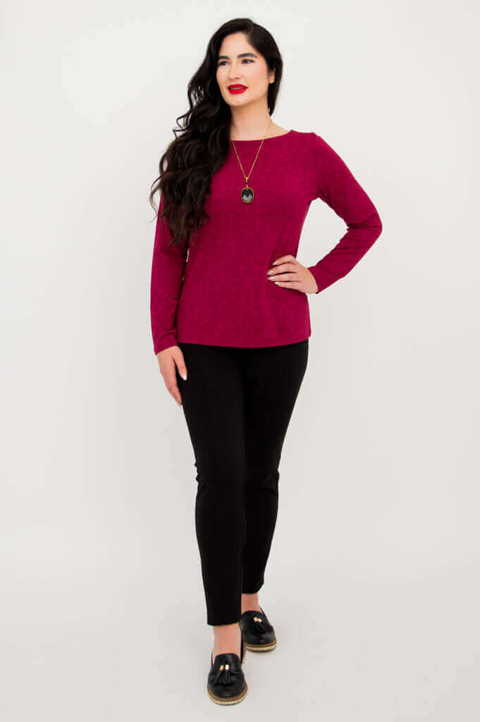 Side-angled standing pose of woman in berry long sleeve top and black pants