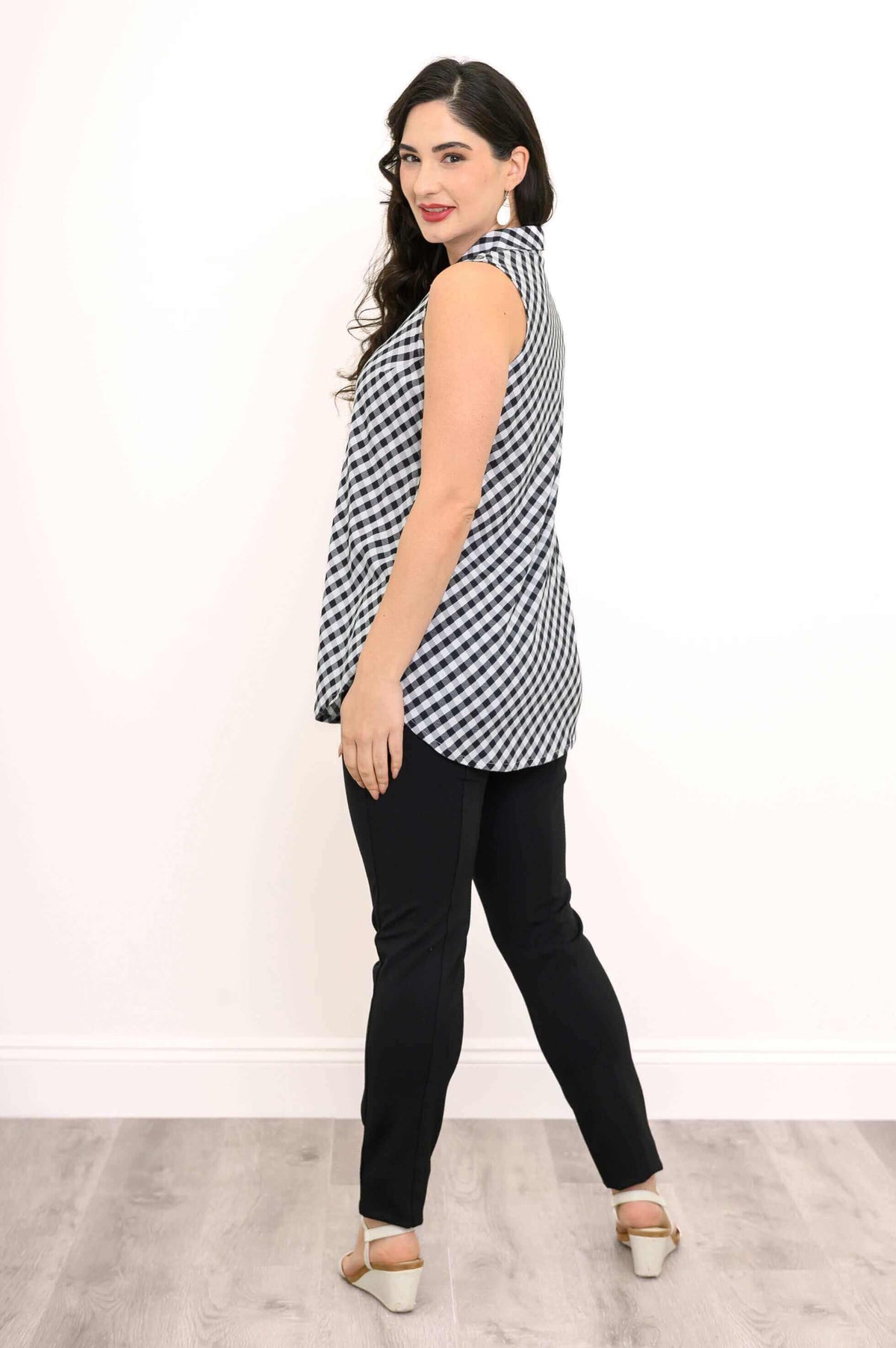 Side-back view of a woman wearing a sleeveless gingham tank top, black pants, and white sandals