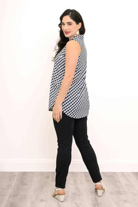 Side-back view of a woman wearing a sleeveless gingham tank top, black pants, and white sandals
