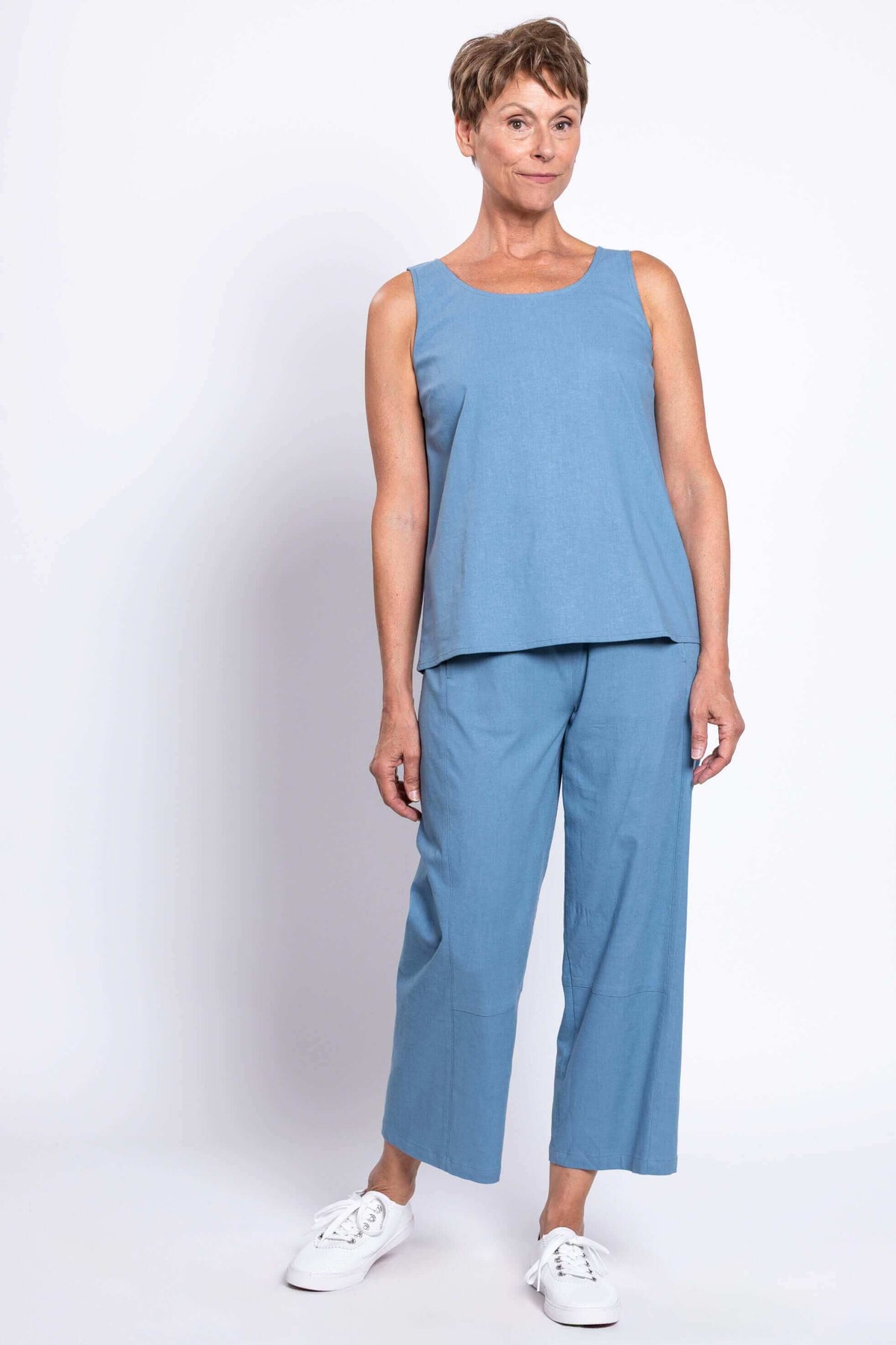 Woman posing in blue sleeveless top and cropped blue pants, turned slightly sideways