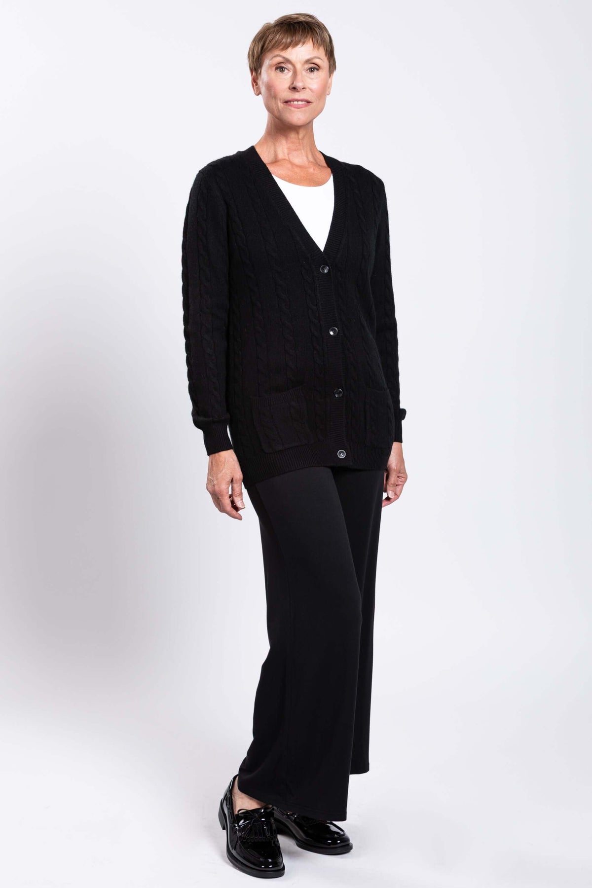 Side angled view of a woman in a black cable knit cardigan and black trousers