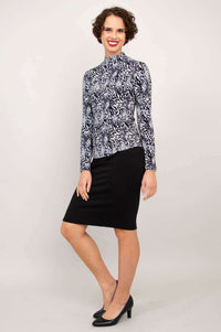 Side-angled view of a woman modeling a black and white palm print mock neck top and black skirt