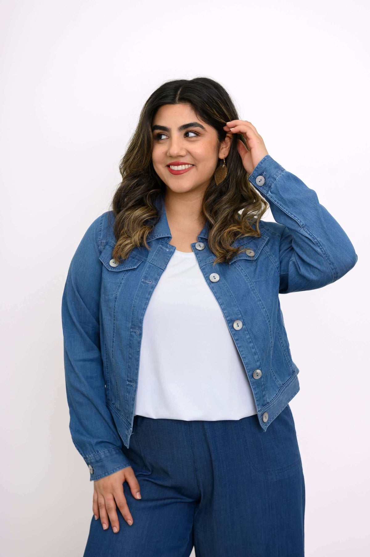 Side angle of a woman adjusting her hair while wearing a blue denim jacket