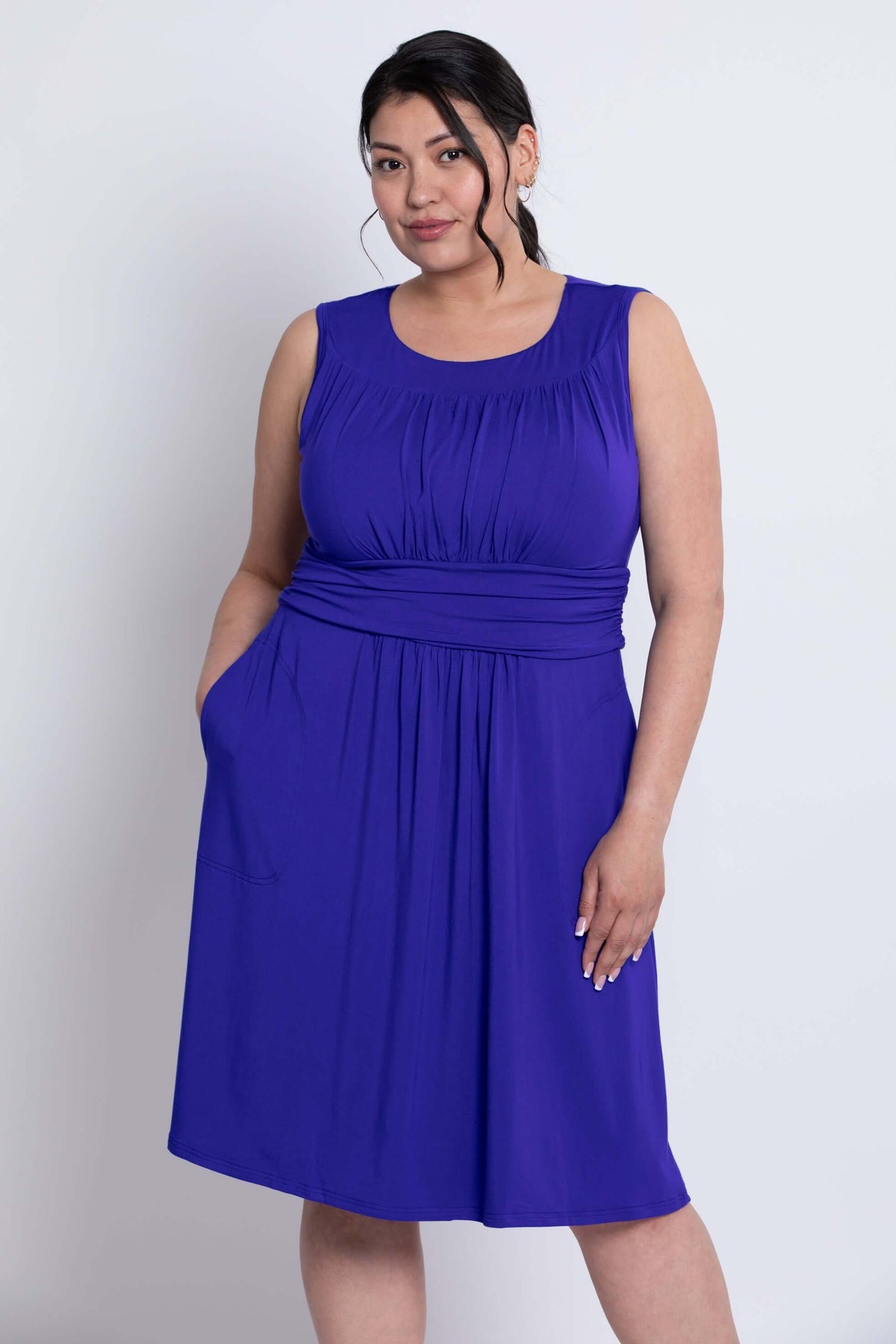 Side angled view of model with hands in pockets wearing purple ruched bamboo dress
