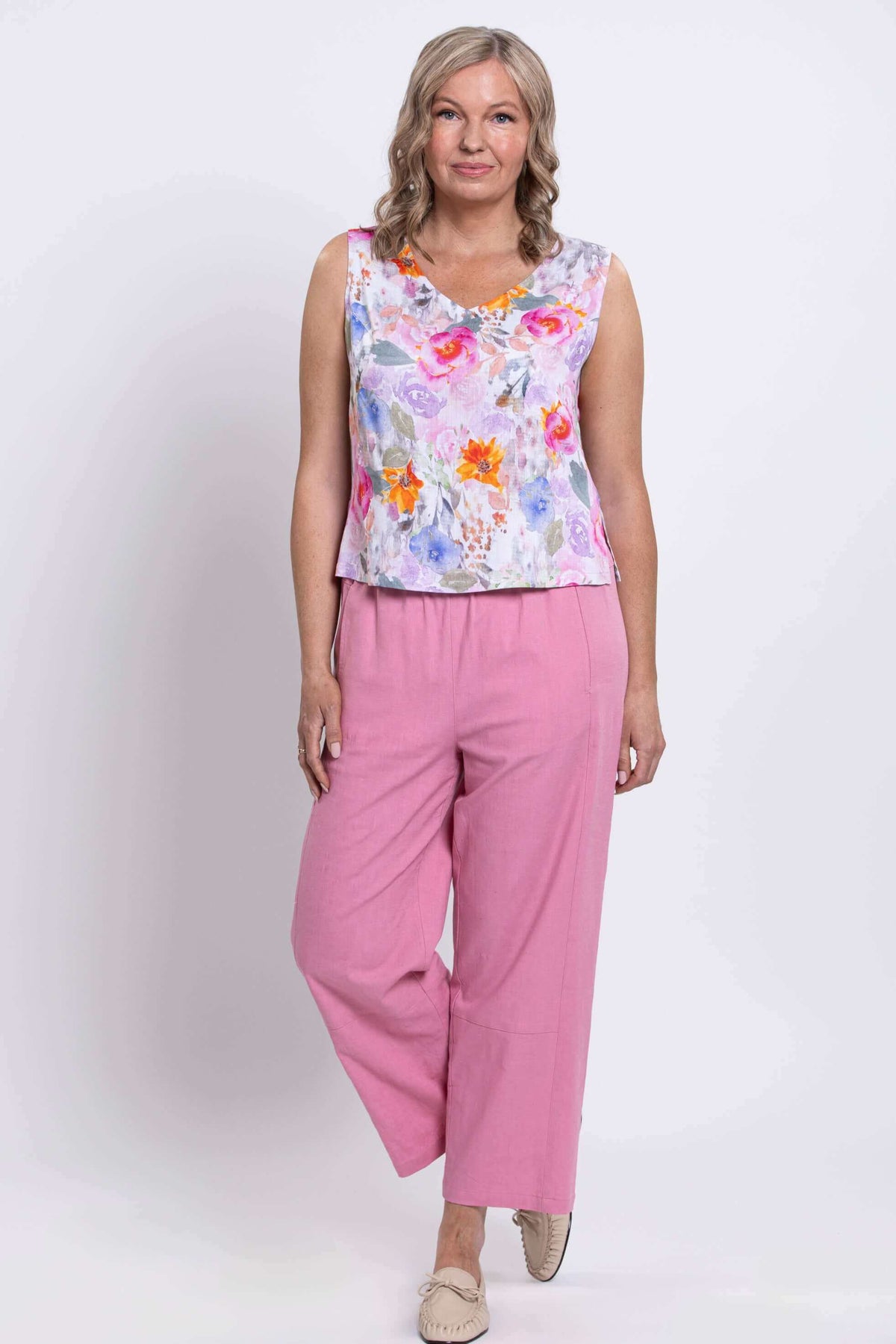 Woman posing with leg bent in floral cropped tank and pink pants