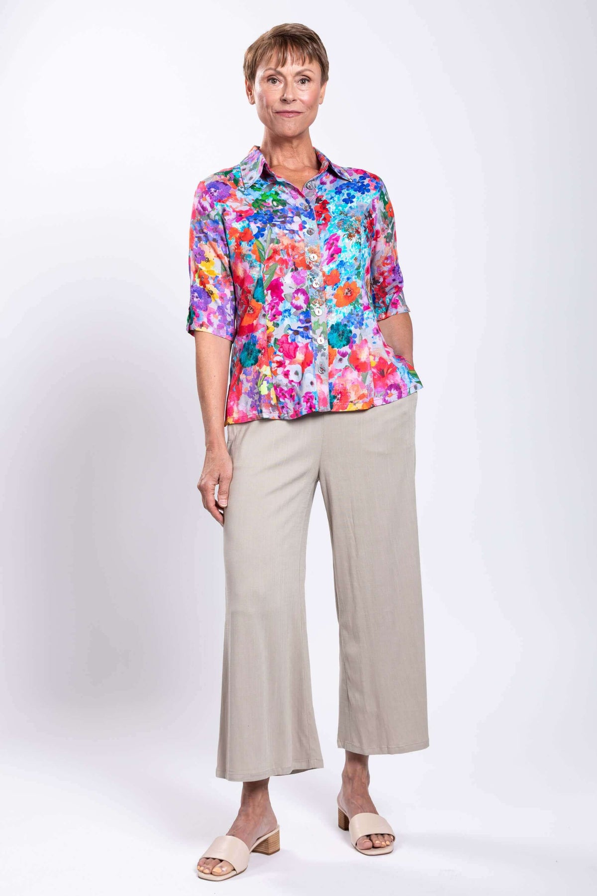 Woman with hand in pocket wearing vivid floral blouse and wide-leg trousers