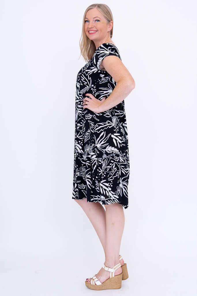 Side view of woman in black and white leafy print dress with hands on hip