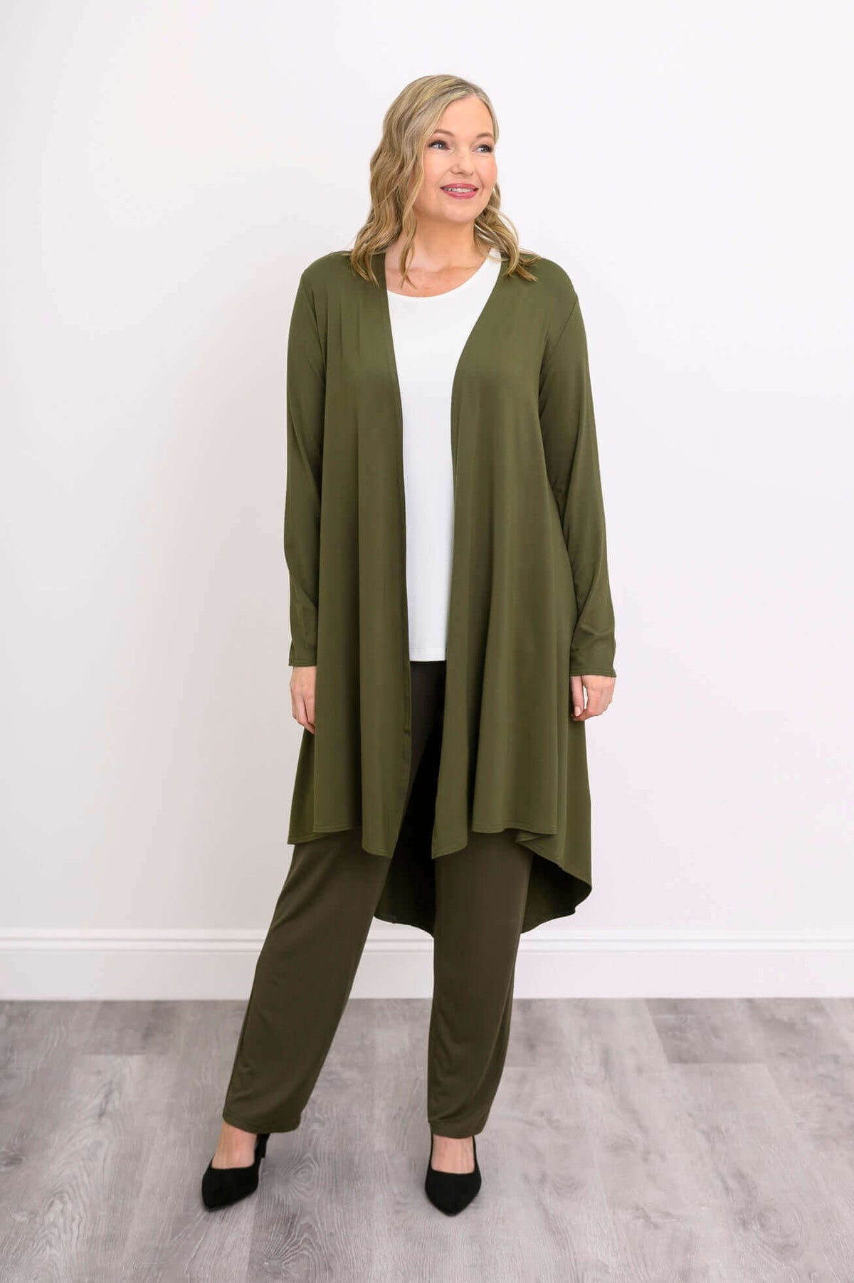 Model looking sideways in olive green high-low duster and pants, hand at side