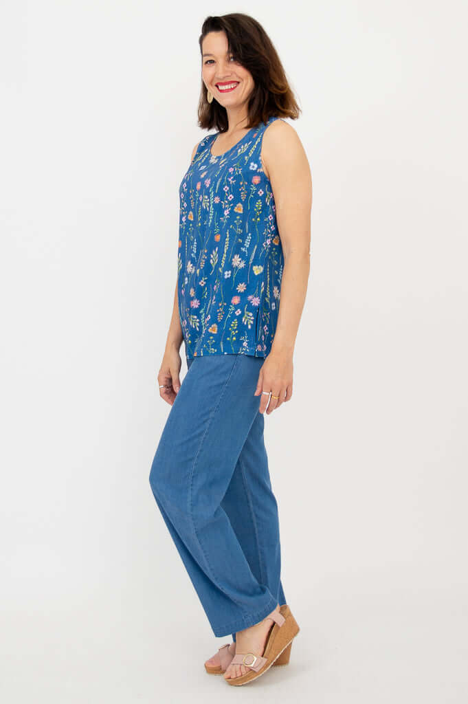Side view of woman in blue floral tank and blue pants, smiling, in wedge sandals