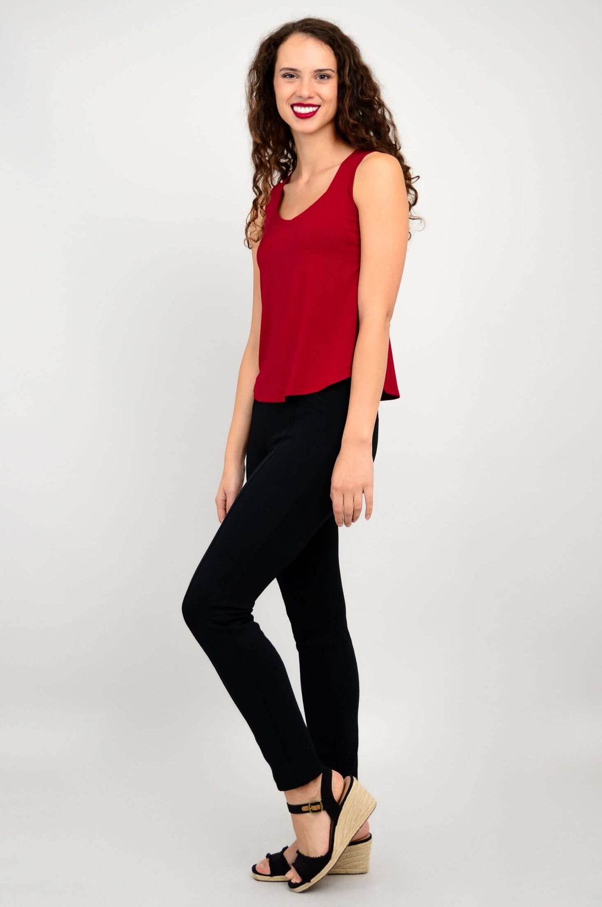 Side view of woman in red tank top and black pants, smiling