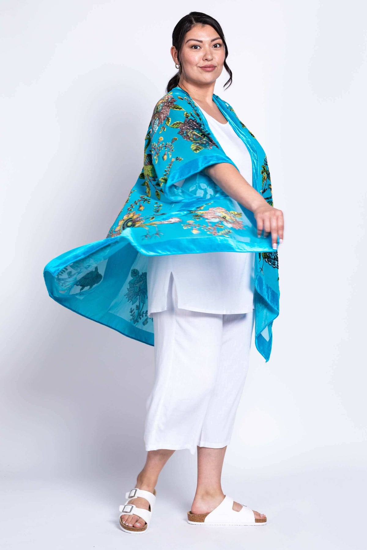 Side view of model twirling in flowing turquoise kimono wrap with floral patterns