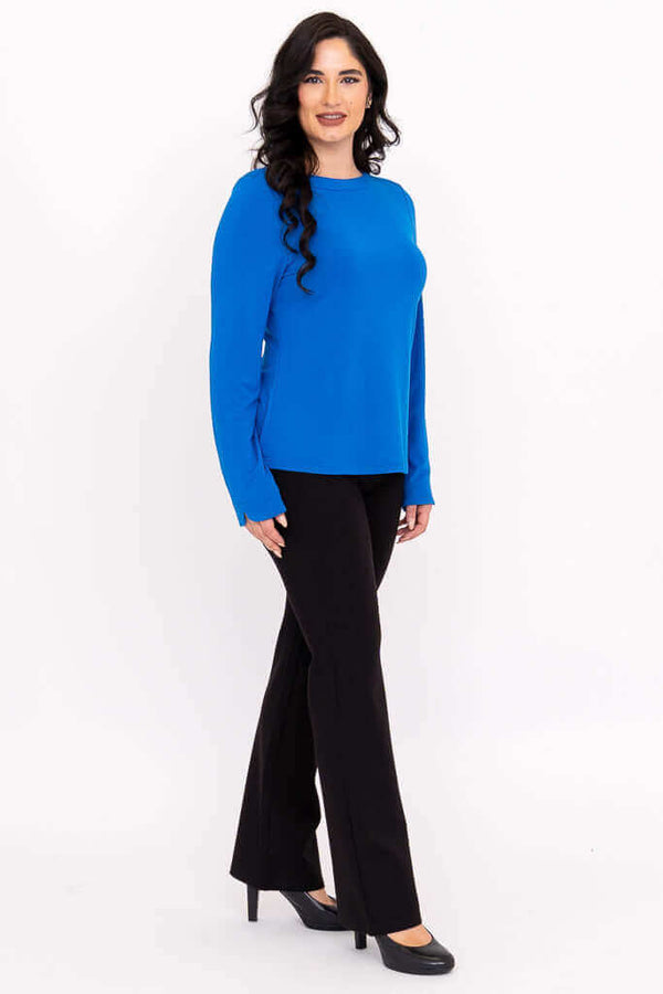 Side view of woman modeling blue boat neck top with black pants and heels