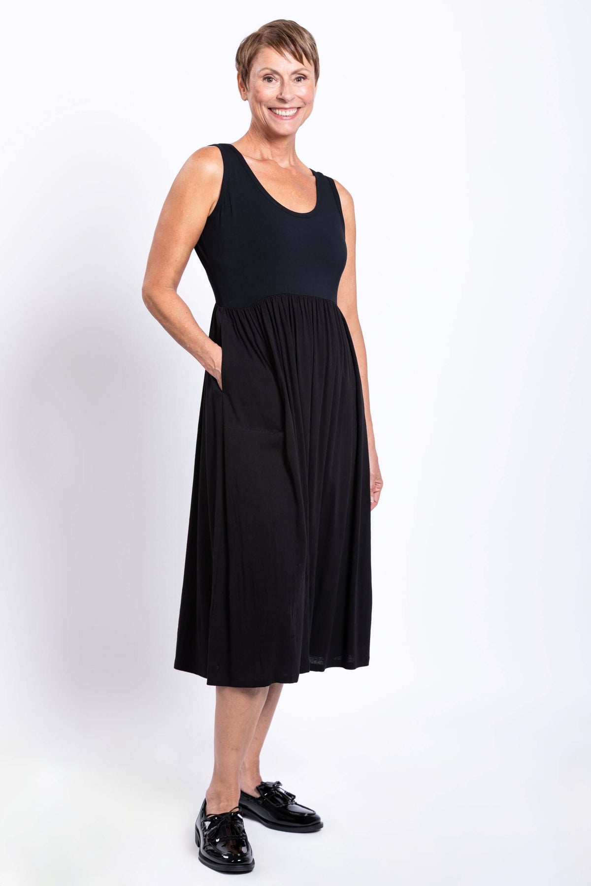 Side view of a model wearing a black empire waist midi dress with pockets